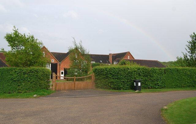 A residential area with a gated driveway, a rainbow, and a black trash bin.