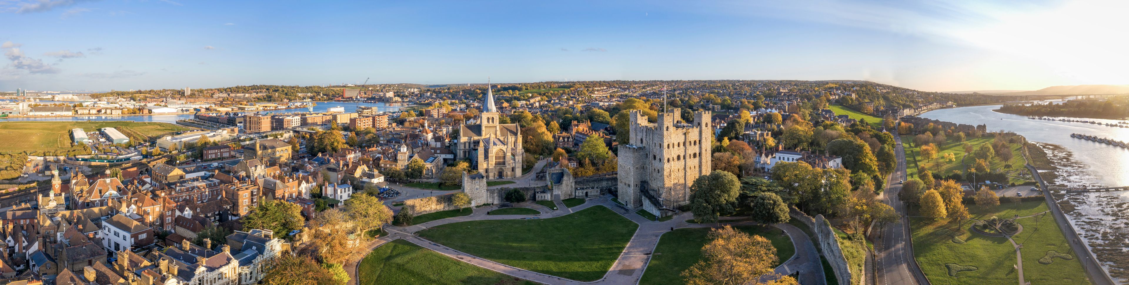 A panoramic view of a historic town with a prominent castle, a river, and surrounding greenery.