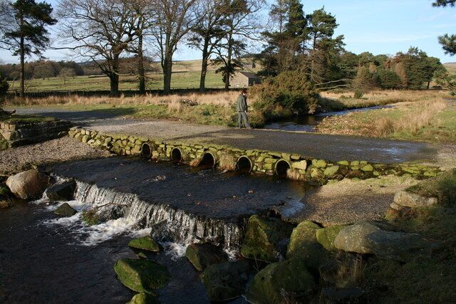 A stone bridge over a stream with a person standing nearby.