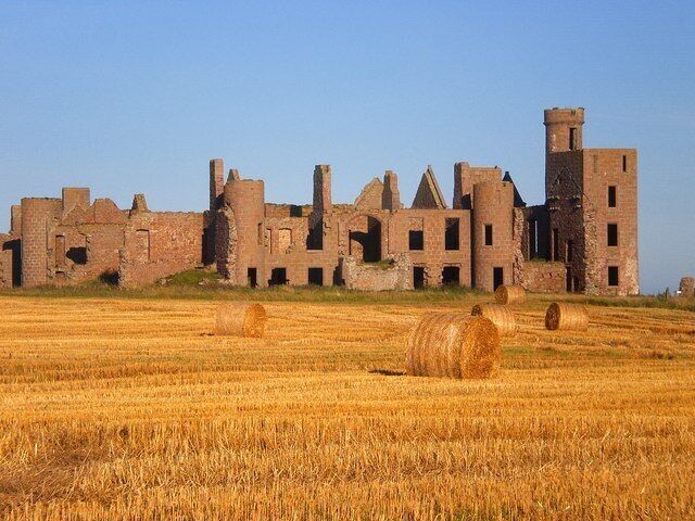 A medieval castle ruins with hay bales in a field.