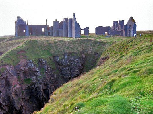 A ruined castle on a grassy hill with a cliffside.