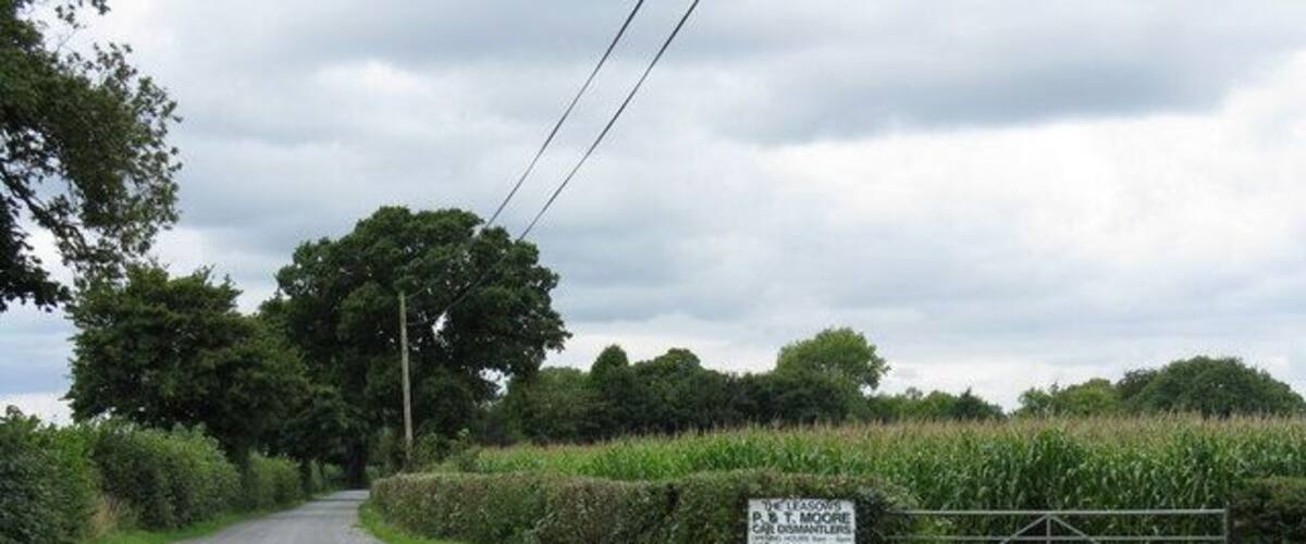 A rural road with a metal gate and a sign indicating 'The Lodge' and 'B.T. Moore'.