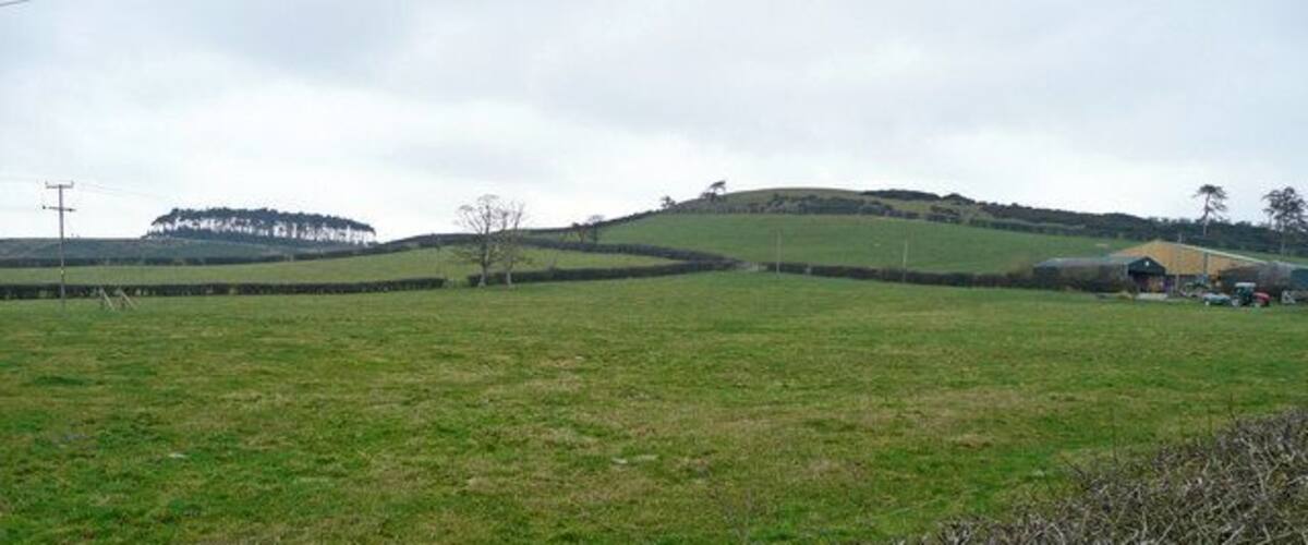 A rural landscape with rolling hills, a field, and a distant building.