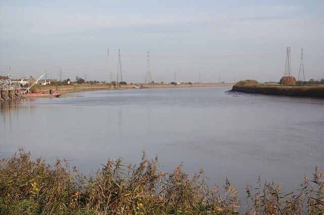 A calm river with a bridge, power lines, and distant buildings.