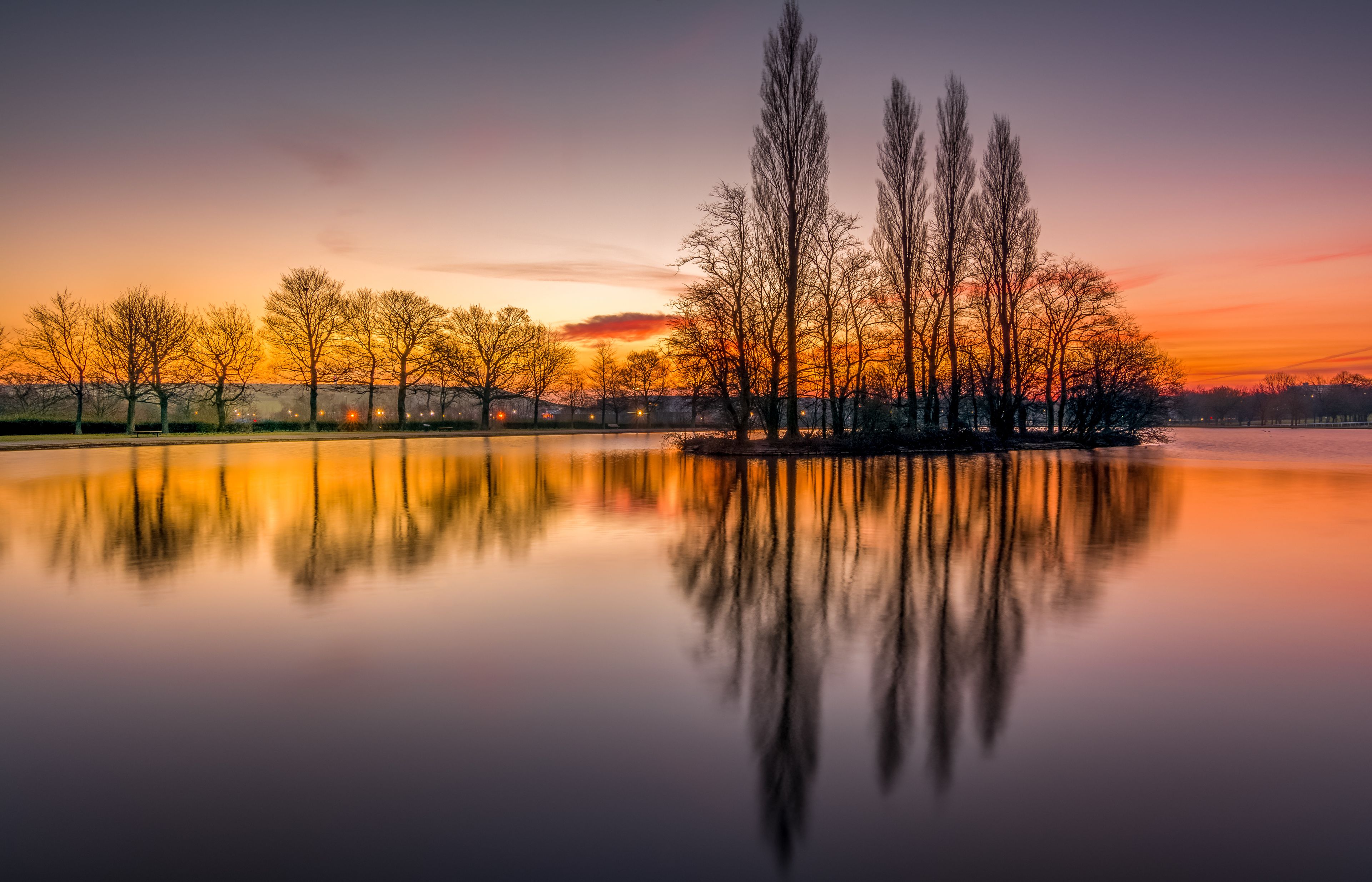 A calm lake reflecting trees and a sunset sky.