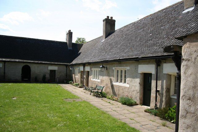 A stone building with a tiled roof, a grassy courtyard, and a bench.