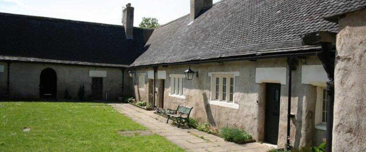 A stone building with a tiled roof, a grassy courtyard, and a bench.