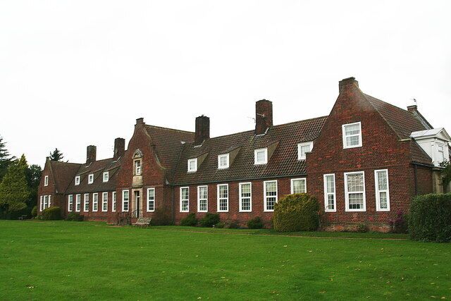 A large brick building with multiple chimneys and windows, surrounded by a well-maintained lawn.