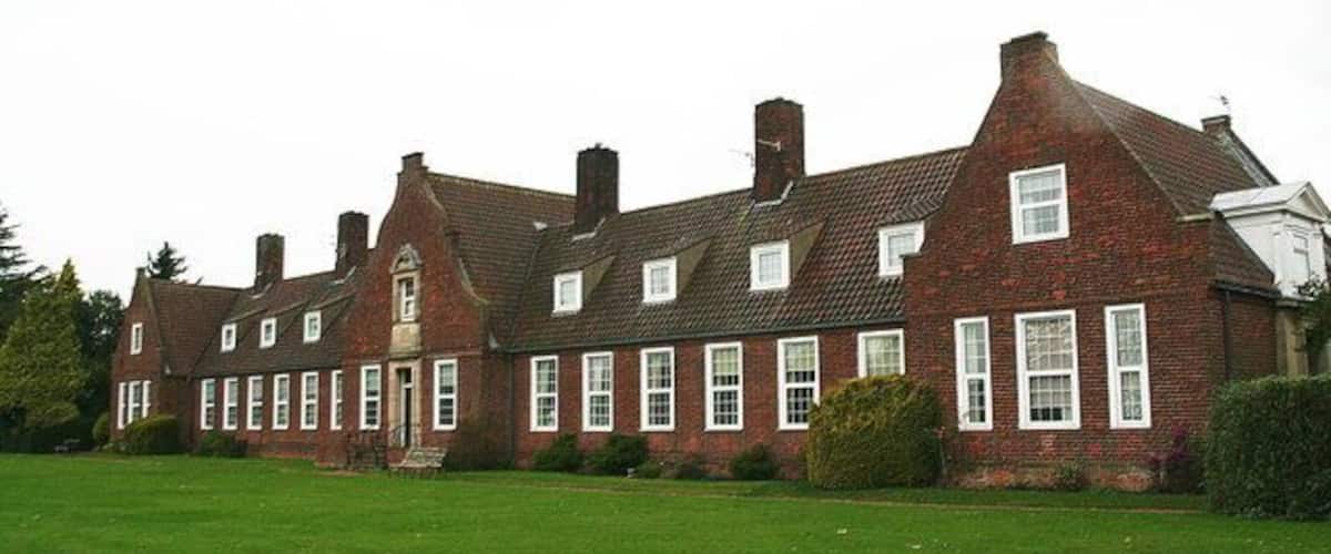 A large brick building with multiple chimneys and windows, surrounded by a well-maintained lawn.