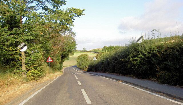 A rural road with a sharp bend, warning signs, and a grassy landscape.