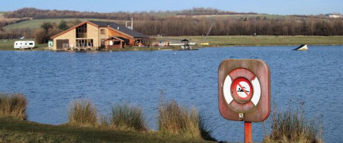 A lake with a house and a no swimming sign.