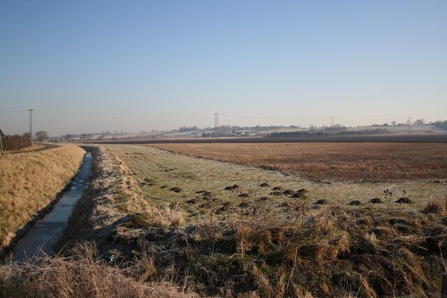 A rural landscape with a narrow water channel, fields, and distant power lines.