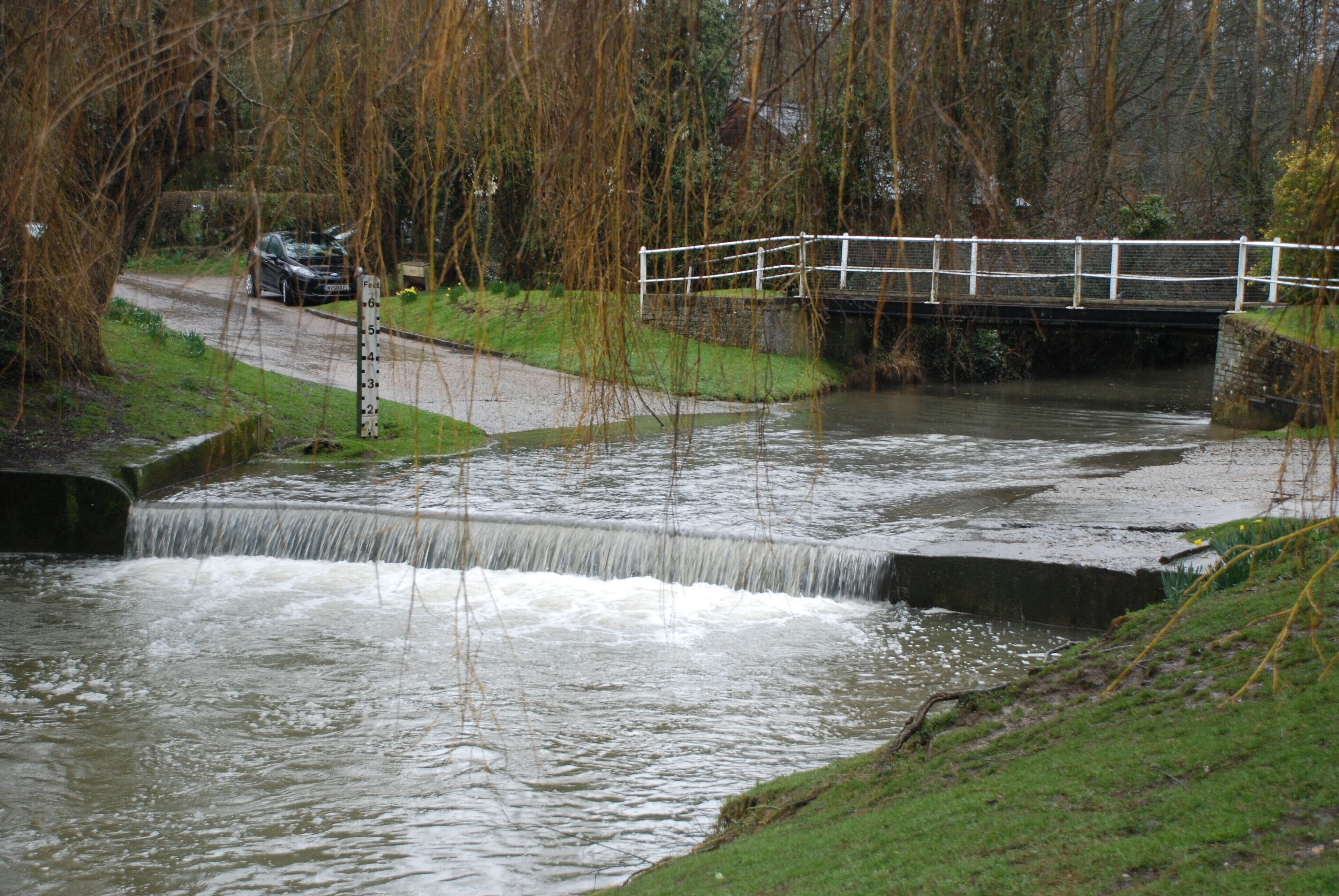 A river flowing under a bridge with a car parked nearby.