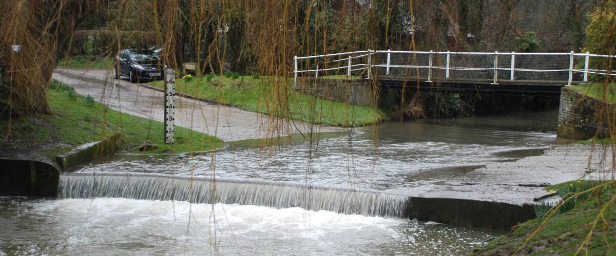 A river flowing under a bridge with a car parked nearby.