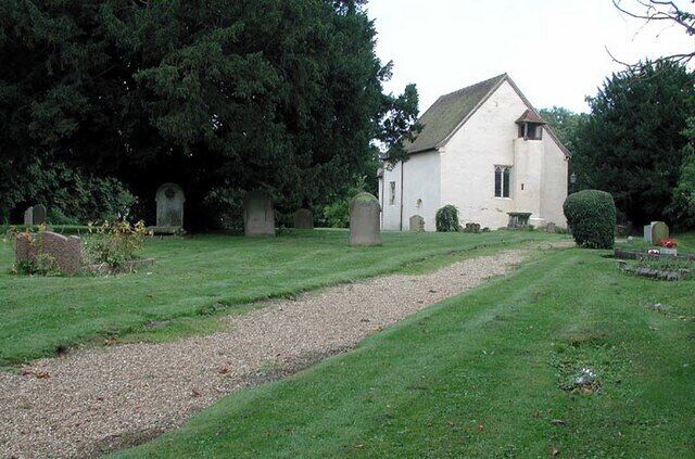 A cemetery with a white church, gravestones, and a gravel path.
