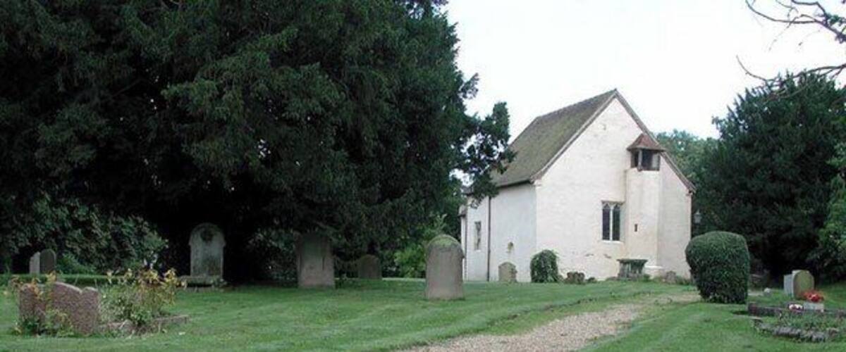 A cemetery with a white church, gravestones, and a gravel path.