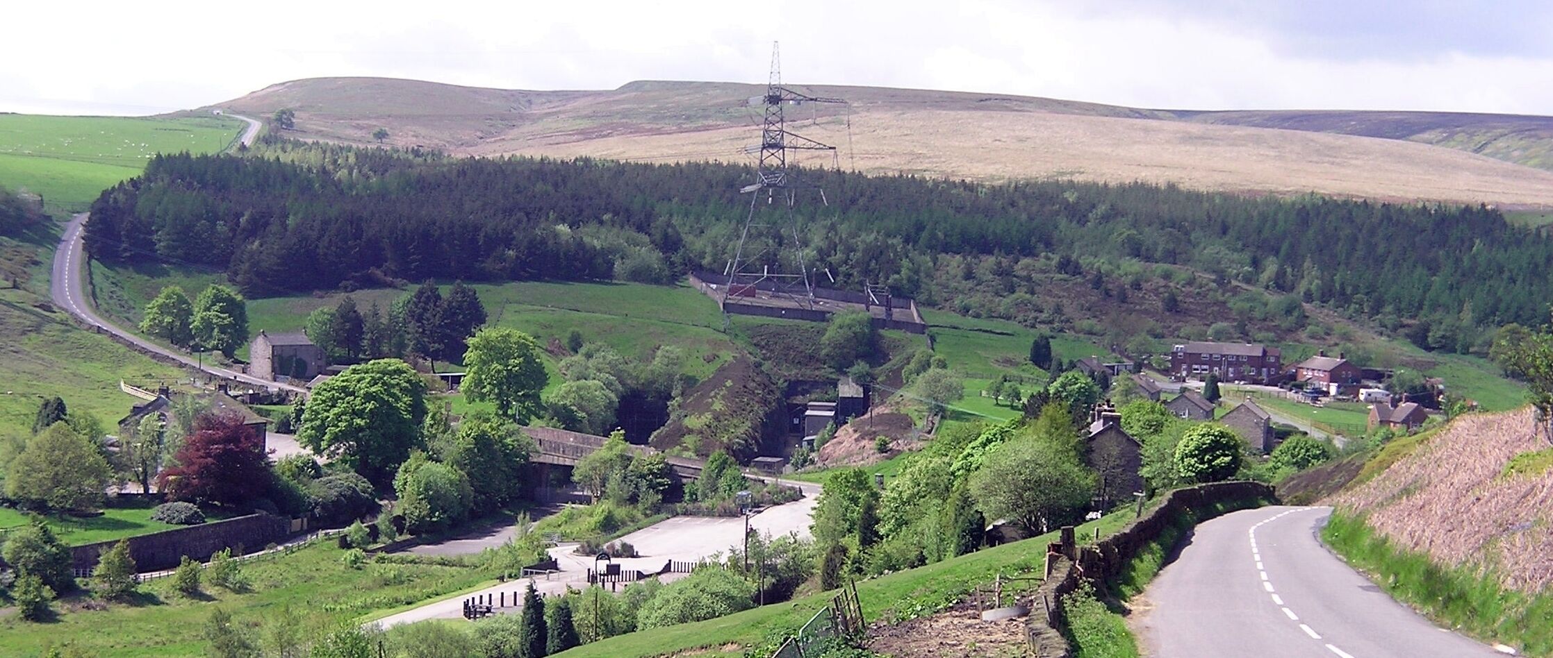 A rural landscape with a winding road, a power line tower, and scattered houses.