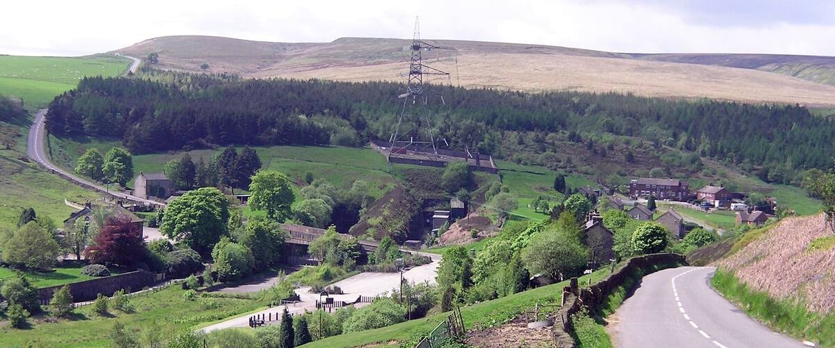 A rural landscape with a winding road, a power line tower, and scattered houses.