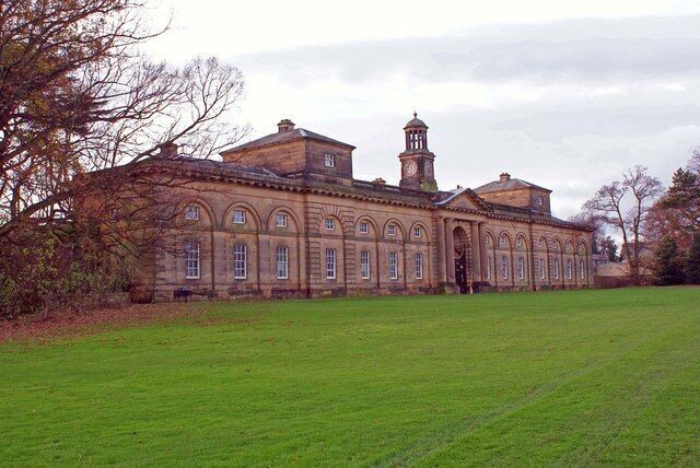 A large, historic building with a clock tower, surrounded by a well-maintained lawn.