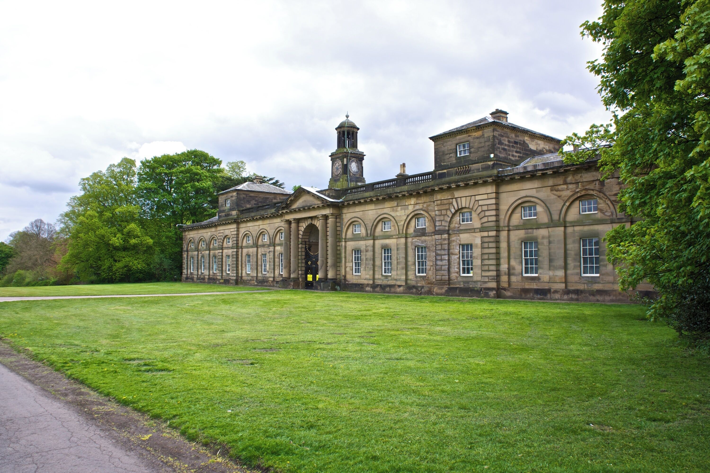 A historic building with a clock tower, arched windows, and a large lawn.