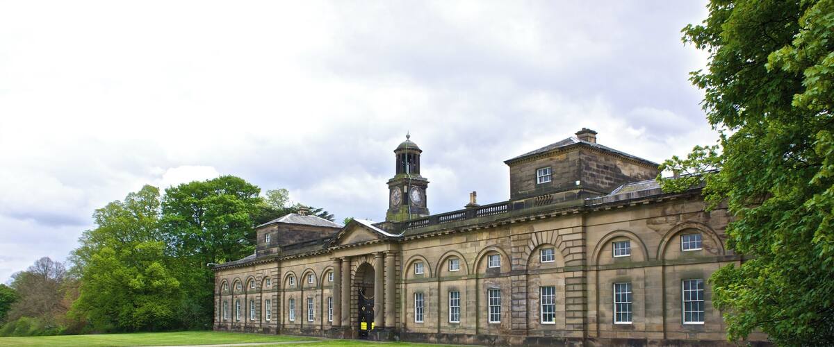 A historic building with a clock tower, arched windows, and a large lawn.
