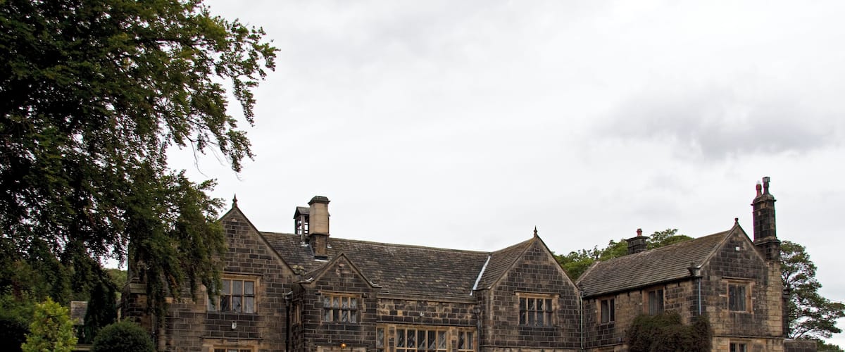 A large stone building with multiple chimneys and windows, surrounded by a well-maintained lawn and flower beds.