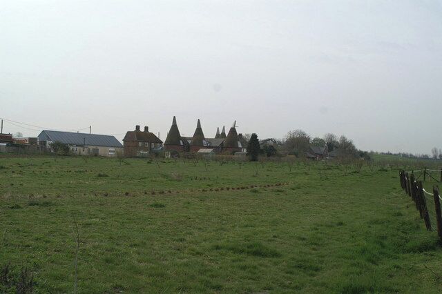 A rural landscape with a field, a fence, and a row of houses with conical roofs.