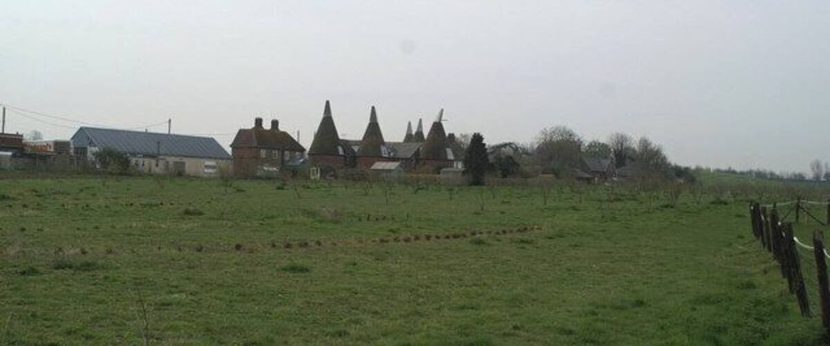 A rural landscape with a field, a fence, and a row of houses with conical roofs.