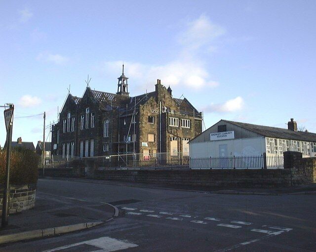 A historic building with a clock tower, a modern extension, and a street in front.