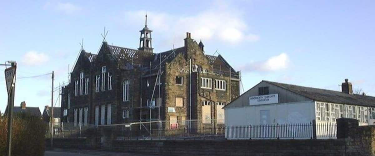 A historic building with a clock tower, a modern extension, and a street in front.