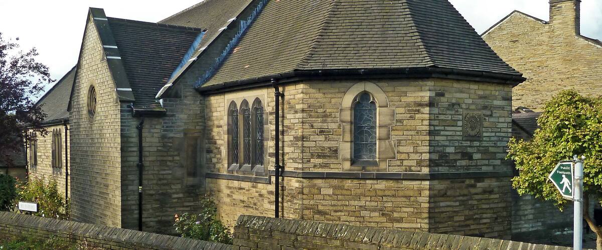 A stone church with a pointed steeple and a cross on top.