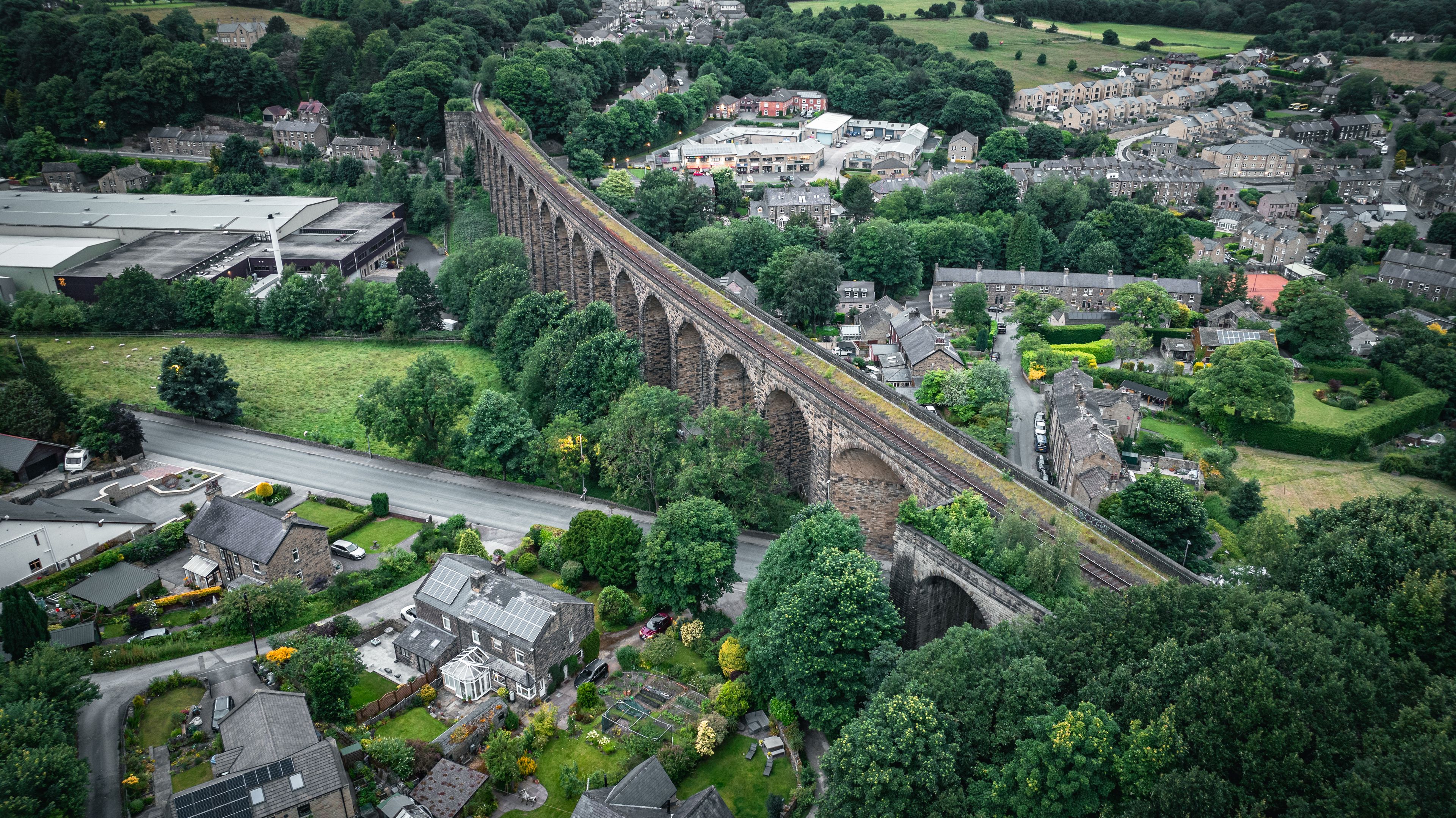An aerial view of a town with a prominent stone viaduct, lush greenery, and residential buildings.
