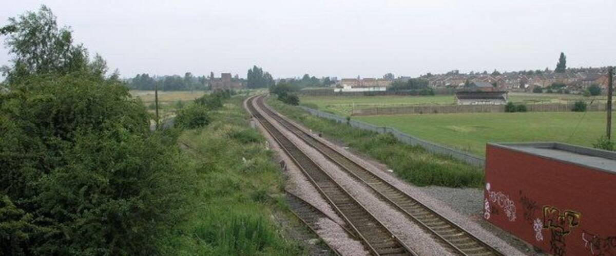 Railway tracks curving through a rural landscape with greenery and a red building with graffiti.
