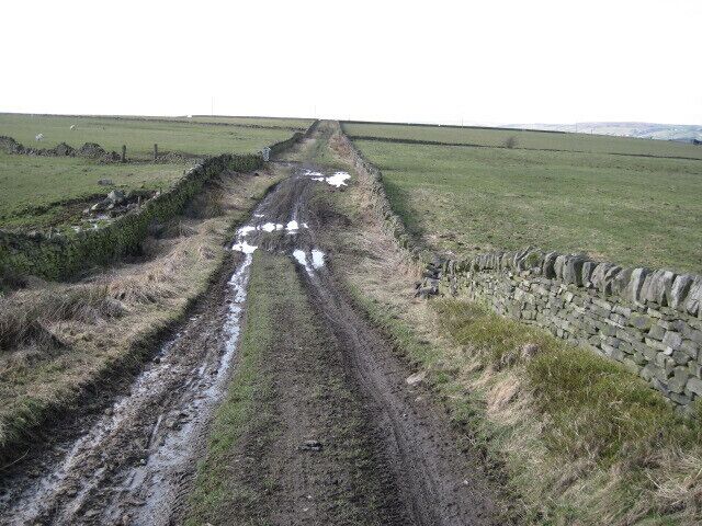 A muddy rural road with puddles, surrounded by stone walls and fields.