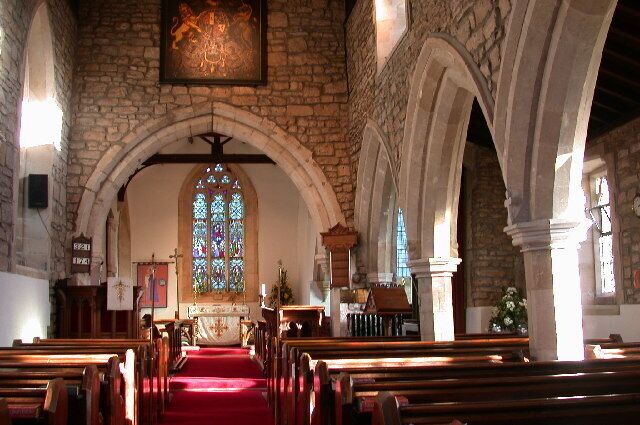 An interior of a church with stone walls, wooden pews, a red carpet, and a stained glass window.