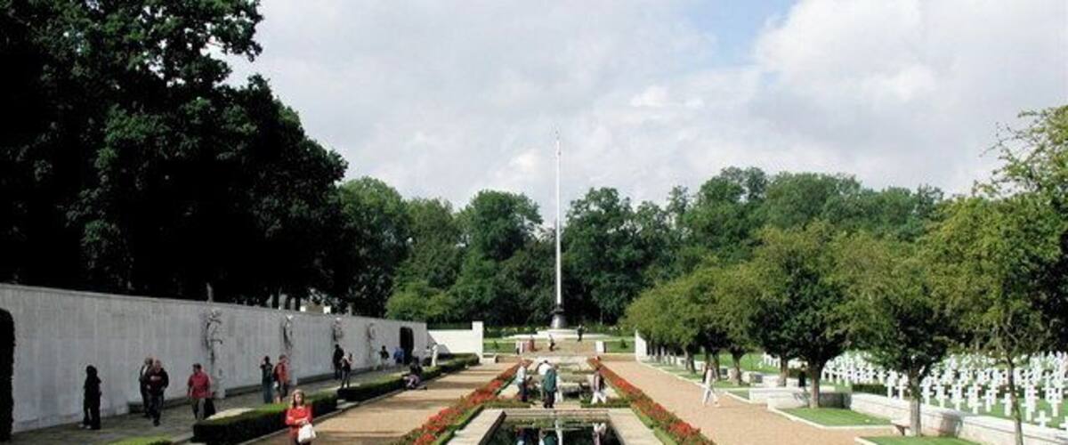 Un parque conmemorativo con un estanque reflectante en el centro, hileras de lápidas y un asta de bandera.