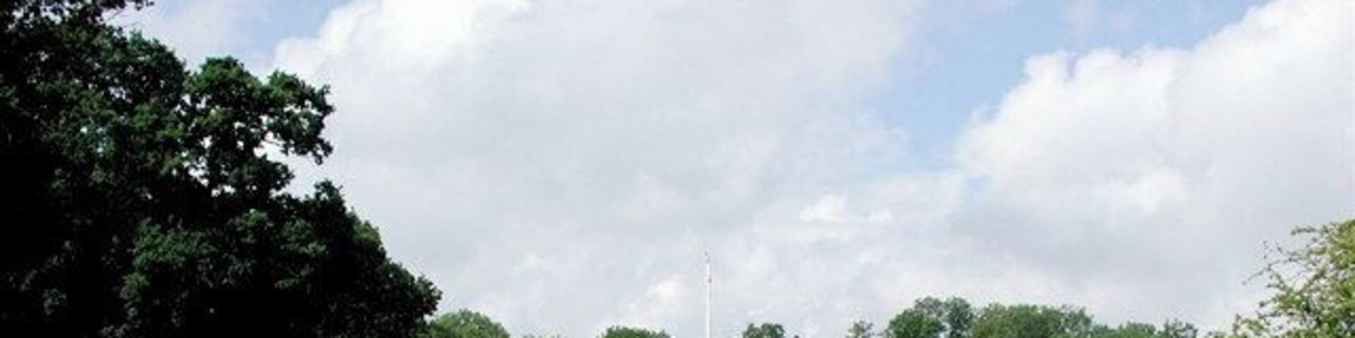 A memorial park with a central reflective pool, rows of graves, and a flagpole.