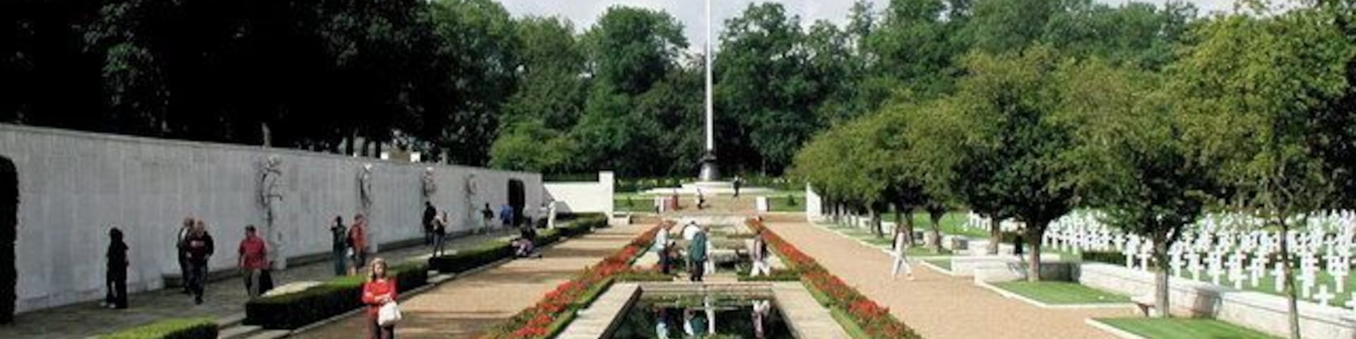 Un parque conmemorativo con un estanque reflectante en el centro, hileras de lápidas y un asta de bandera.