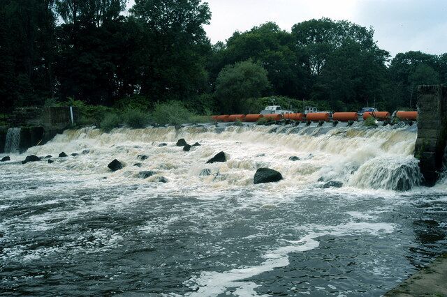 A river with a dam and rocks, surrounded by trees.