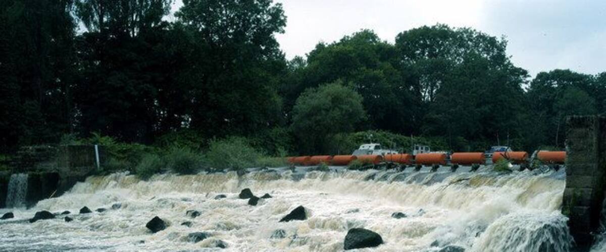 A river with a dam and rocks, surrounded by trees.
