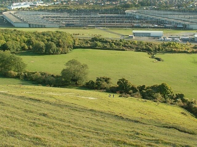 People climbing to the White Horse on Cheriton Hill Looking down the steep hill from the viewpoint on Crete Road West. Part of the Eurotunnel rail terminal is seen below.