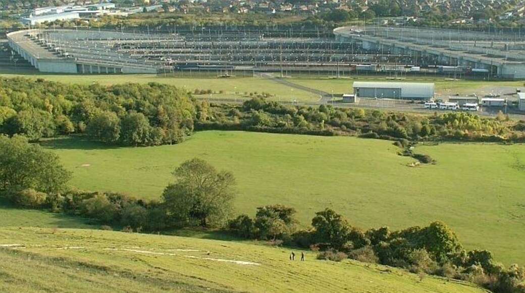 People climbing to the White Horse on Cheriton Hill Looking down the steep hill from the viewpoint on Crete Road West. Part of the Eurotunnel rail terminal is seen below.