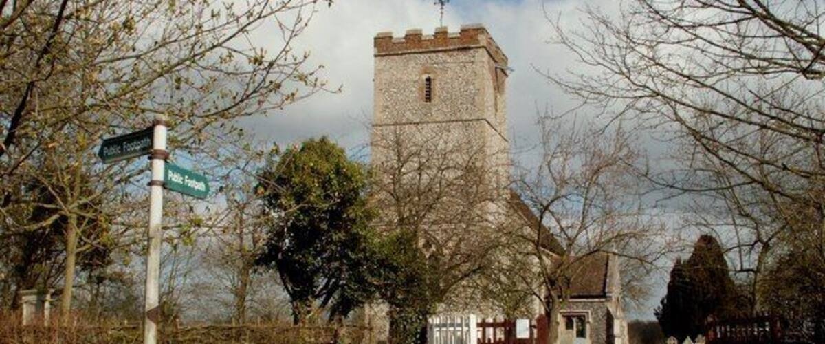 A rural road leading to a stone church with a tower, surrounded by trees and daffodils.