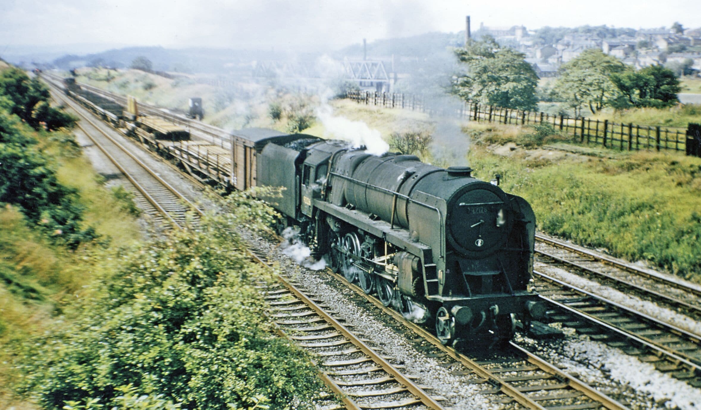 A steam locomotive on railway tracks with a town in the background.