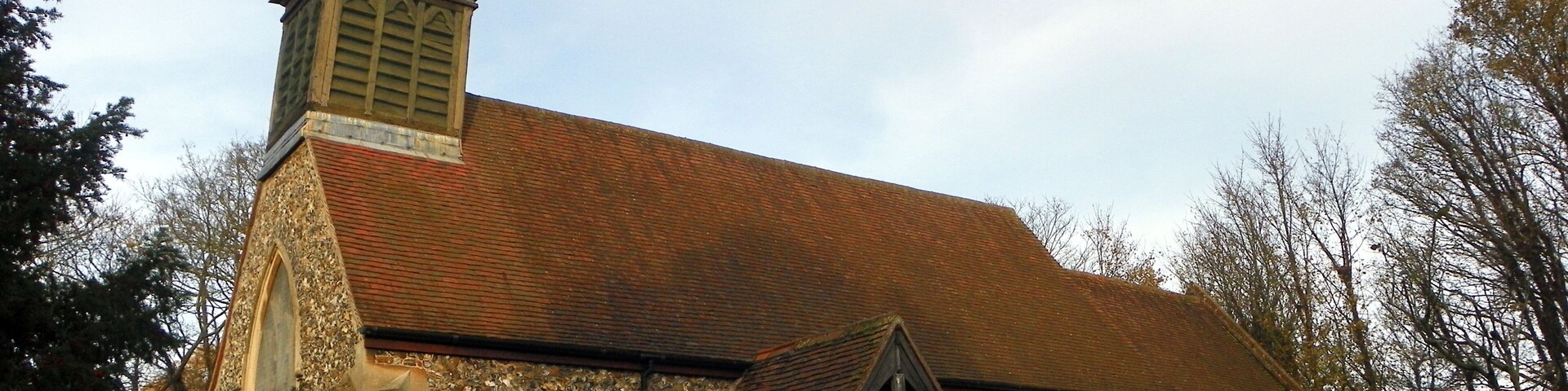 A church with a stone facade, a red-tiled roof, and a pointed steeple.