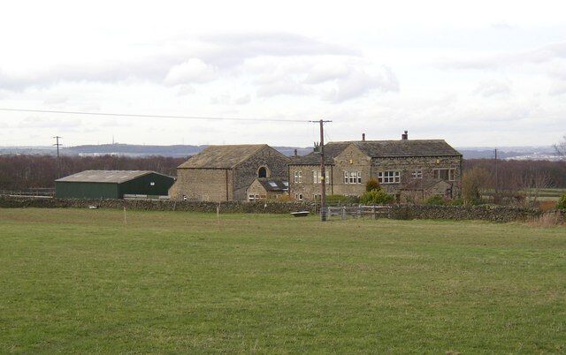 A rural landscape with a stone house, a green barn, and open fields.