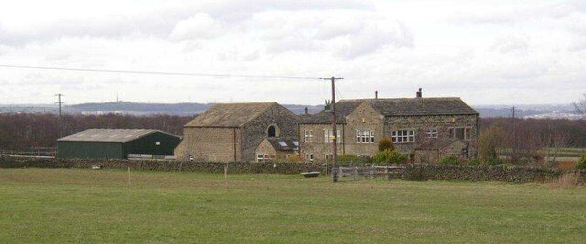 A rural landscape with a stone house, a green barn, and open fields.
