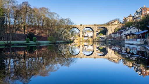 Un puente de piedra sobre un río tranquilo, rodeado de árboles y edificios.