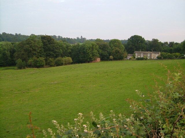 A green field with a house in the distance.