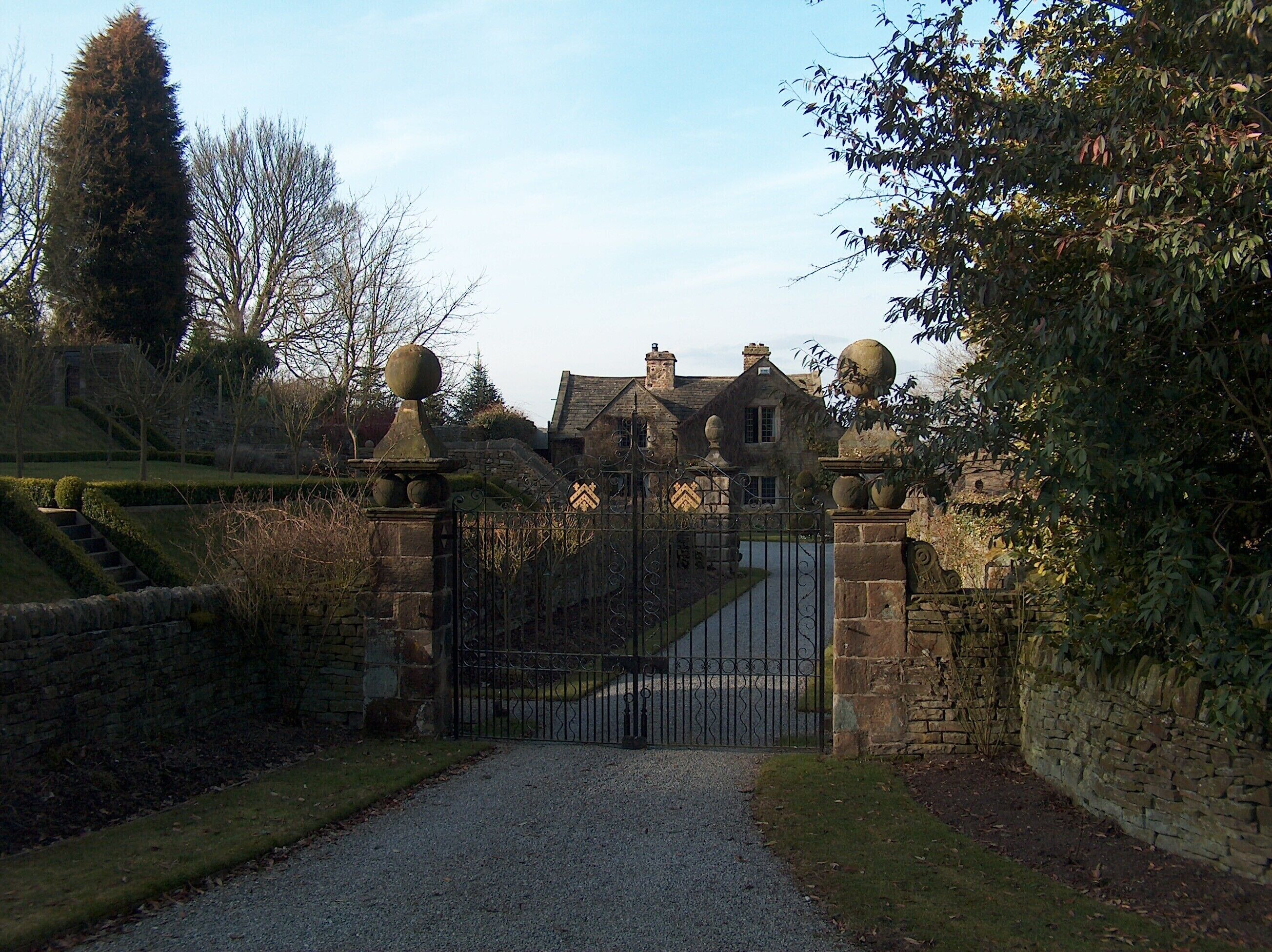 A gated entrance to a historic building with stone walls and a gravel path leading to it.